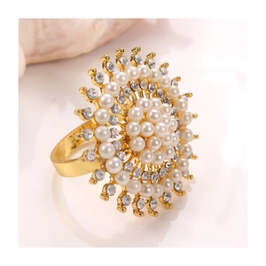 Golden flower napkin ring with pearls and rhinestones on a white reflective surface