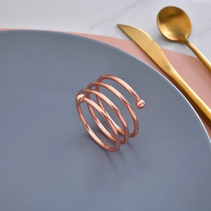 Rose gold spiral metal napkin ring with ball ends on a matte ceramic plate