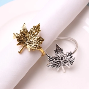 Detailed macro view of gold and silver metallic maple leaf napkin rings on white fabric