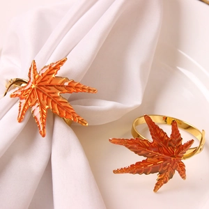 Golden maple leaf napkin rings with orange enamel finish on white fabric and plate