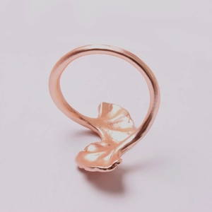 Close-up of rose gold ginkgo leaf napkin ring with detailed vein texture on pink background