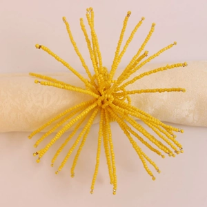 Détail d'un rond de serviette en perles jaunes avec motif rayon de soleil et pompon