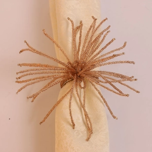 Détail d'un rond de serviette perlé avec pompon doré sur une serviette en damas beige