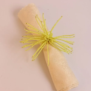 Détail d'un rond de serviette en perles jaunes avec motif rayon de soleil et anneau doré