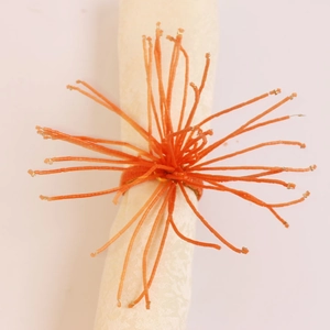 Détail d'un rond de serviette à perles orange avec accents dorés sur serviette blanche