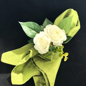 Close-up of white silk roses and green leaves on a wedding napkin ring holder