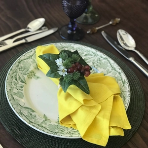 Detail of white rose napkin ring with green leaves and berries on a yellow fabric napkin