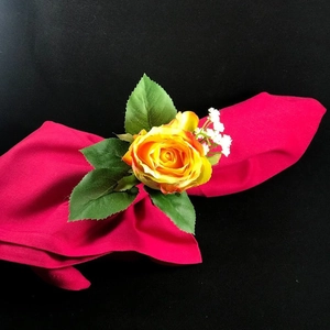 Detailed view of yellow rose napkin ring with green leaves on a red fabric napkin