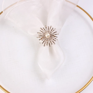 Dettaglio di un portatovagliolo dorato con perle e cristalli su un piatto bianco