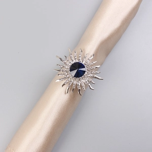 Detail shot of a silver sunflower napkin ring with a deep blue gemstone on champagne silk