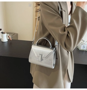 Sac à main trapèze argenté avec poignée et fermoir rotatif porté par un mannequin