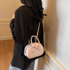 Pink bow-knot bowling handbag with crossbody strap shown by model in minimalist setting
