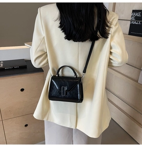Détail d'un sac bandoulière noir brillant plissé sur un blazer avec boucle argentée