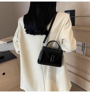 Détail d'un sac minimaliste en cuir synthétique noir avec boucle en métal sur un costume beige