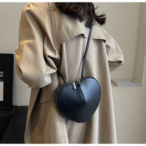 Dettaglio di una borsa a tracolla nera a forma di cuore indossata su un trench beige