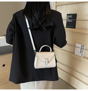 Détail du mini sac à bandoulière en cuir blanc crème porté sur un blazer noir élégant