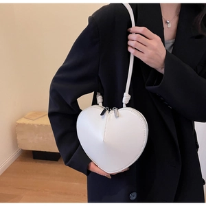 Borsa a tracolla bianca a forma di cuore indossata su un blazer nero per contrasto