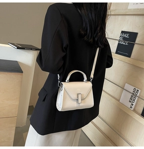 Détail d'un sac à main minimaliste blanc crème avec boucle argentée porté par un modèle