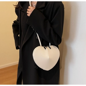 Dettaglio di una borsa bianca a forma di cuore indossata da una modella con cappotto