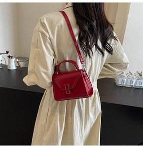 Détail d'un sac à main rouge avec fermoir argenté porté avec un trench-coat chic