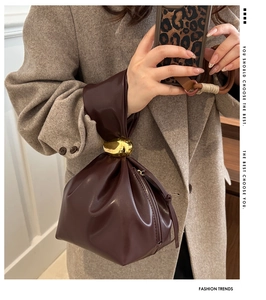 Detail of burgundy pleated bucket bag featuring an artistic gold knotted metal buckle