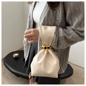 Detail of cream pleated leather bucket bag featuring a large fluid gold metal buckle
