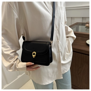 Fashionable black leather crossbody square bag with gold buckle shown on casual outfit