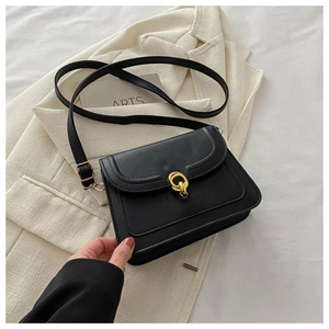 Close-up of black minimalist crossbody bag with gold double-ring buckle on a blazer