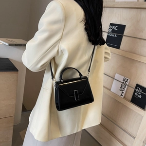 Sac à main chic noir brillant avec fermoir argenté porté dans un cadre professionnel
