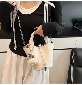 Detail of off-white bucket bag with lychee grain texture, metal chain, and heart pendant