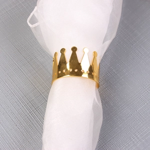Detailed close-up of golden crown napkin ring with polished finish on white mesh fabric