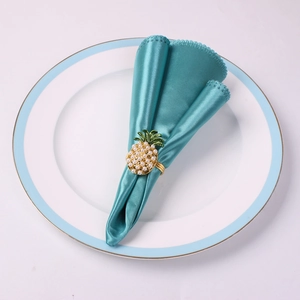 Détail d'un rond de serviette ananas doré avec perles blanches et feuilles vertes sur tissu
