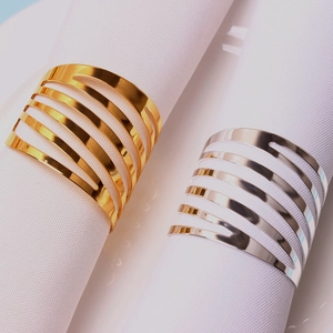Close-up of gold and silver napkin rings with parallel striped lines on white fabric