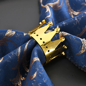 Polished gold crown napkin ring holder with hollow design on blue luxury fabric napkin