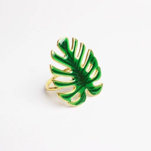 Détail d'un rond de serviette doré avec une feuille de Monstera tropicale en émail vert
