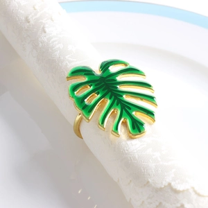 Détail d'un rond de serviette feuille de Monstera dorée et émail vert sur tissu blanc