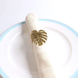 Gros plan d'un rond de serviette feuille de monstera dorée sur une serviette et une assiette