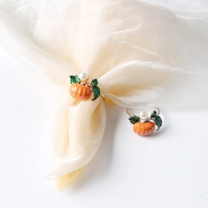 Macro shot of pumpkin napkin rings with orange enamel and pearls on silk fabric