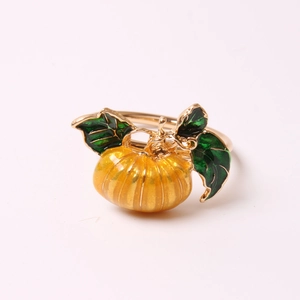 Detailed close-up of an orange enamel pumpkin napkin ring with golden base and green leaves
