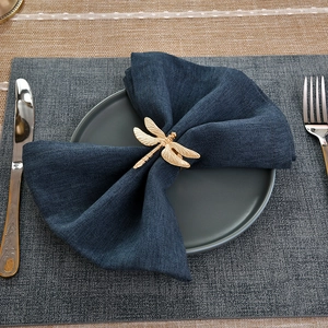 Golden dragonfly napkin ring with textured wings on a dark blue linen napkin