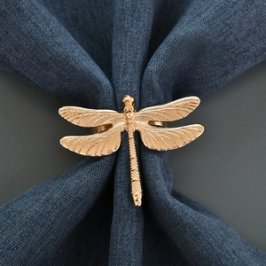 Golden dragonfly napkin ring with textured wings on dark blue cloth backdrop