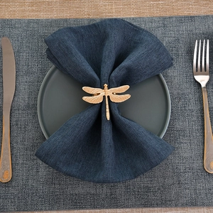 Close-up of golden dragonfly napkin ring with intricate wing texture on blue linen