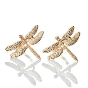 Close-up of two golden dragonfly napkin rings with detailed wing texture on white background