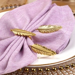 Ronds de serviette en forme de plumes dorées sur du linge violet et plateau en céramique