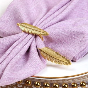 Rond de serviette plume dorée sur serviette en lin violette pour décor de luxe
