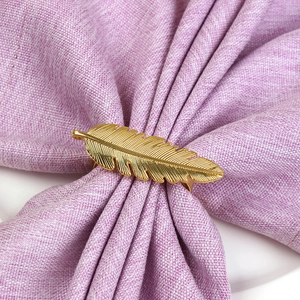Détail d'un rond de serviette doré en forme de plume sur un tissu en lin violet chic