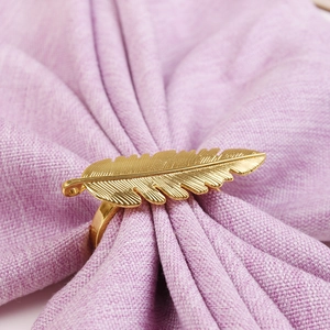 Gros plan du rond de serviette doré en forme de plume sur un tissu en lin violet