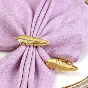 Rond de serviette en métal doré en forme de plume sur une serviette en lin mauve