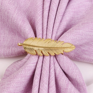 Détail macro du rond de serviette plume dorée sur un tissu texturé violet