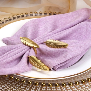 Détail de ronds de serviette plumes dorées avec des textures fines sur lin doux